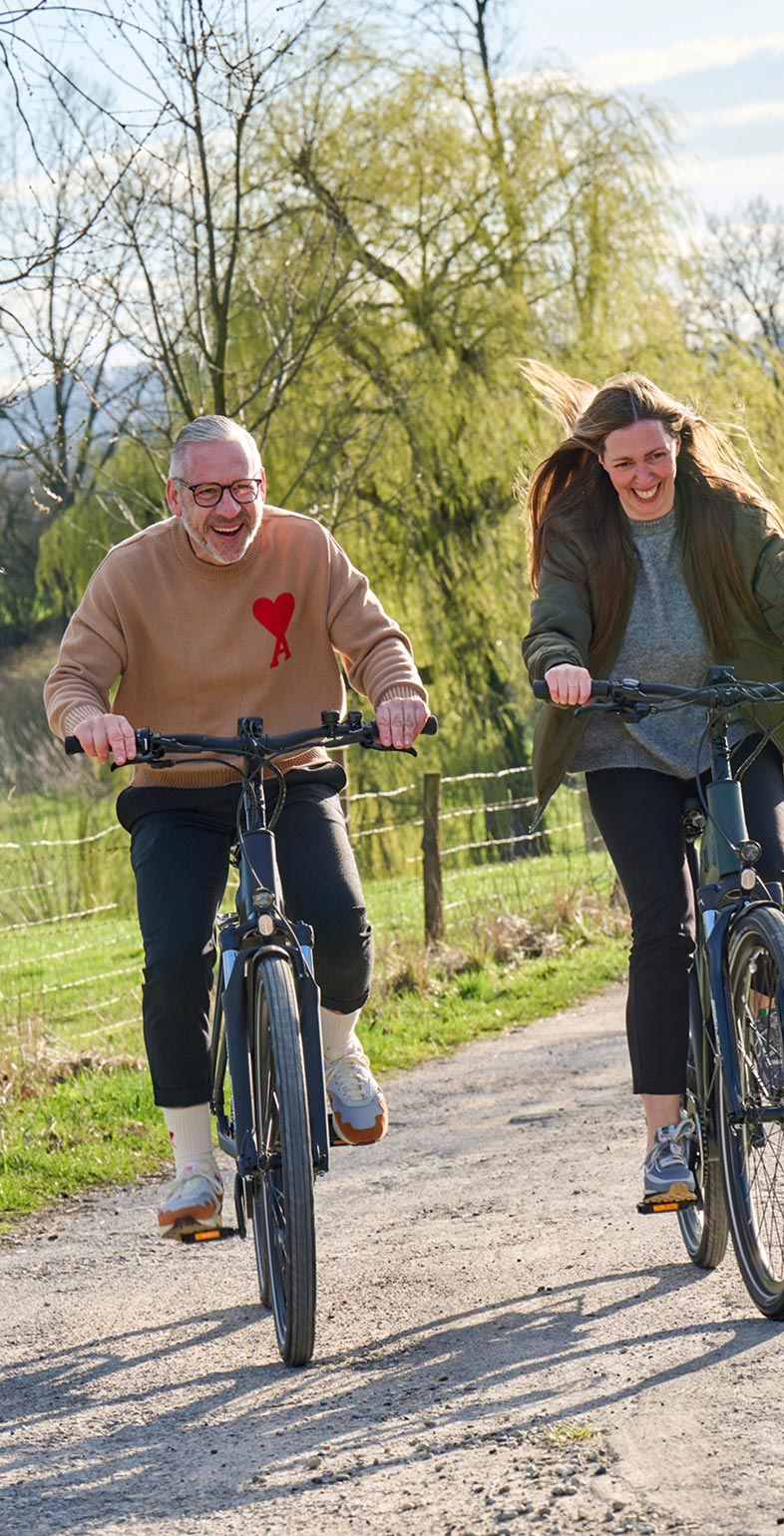 Zwei Personen fahren fröhlich E-Bike auf einem Feldweg – Lifestyle-Visual für Wittich Bikes, entwickelt von Neue Identität. Fotografie Sebi Ruthe.