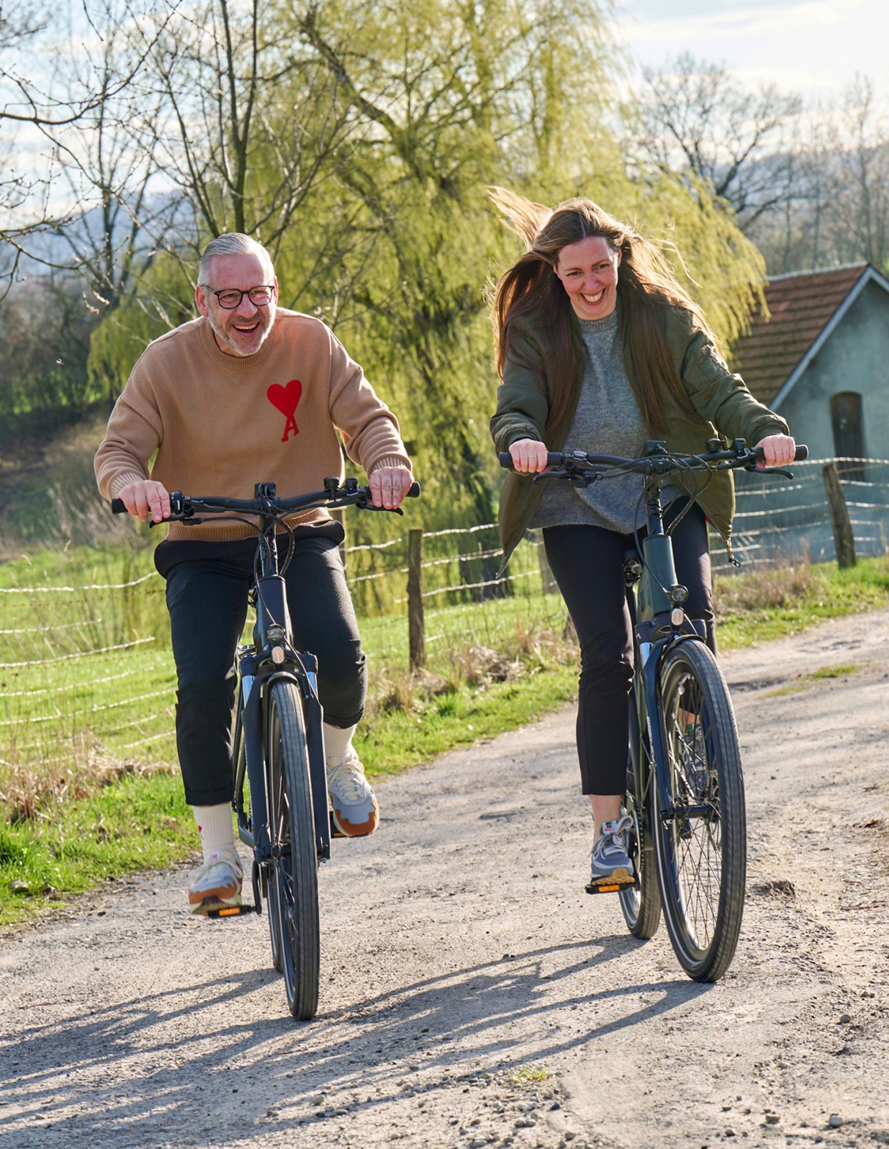 Zwei Personen fahren fröhlich E-Bike auf einem Feldweg – Lifestyle-Visual für Wittich Bikes, entwickelt von Neue Identität. Fotografie Sebi Ruthe.